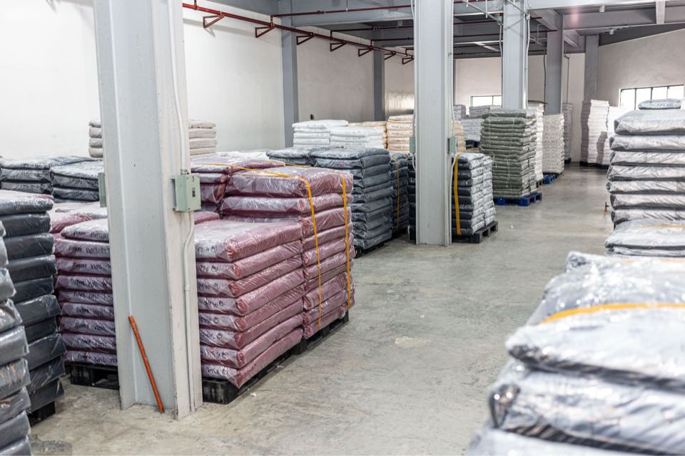 Wrapped rolls of pink and grey knitted fabric stacked on pallets between the columns of the fabric store.
