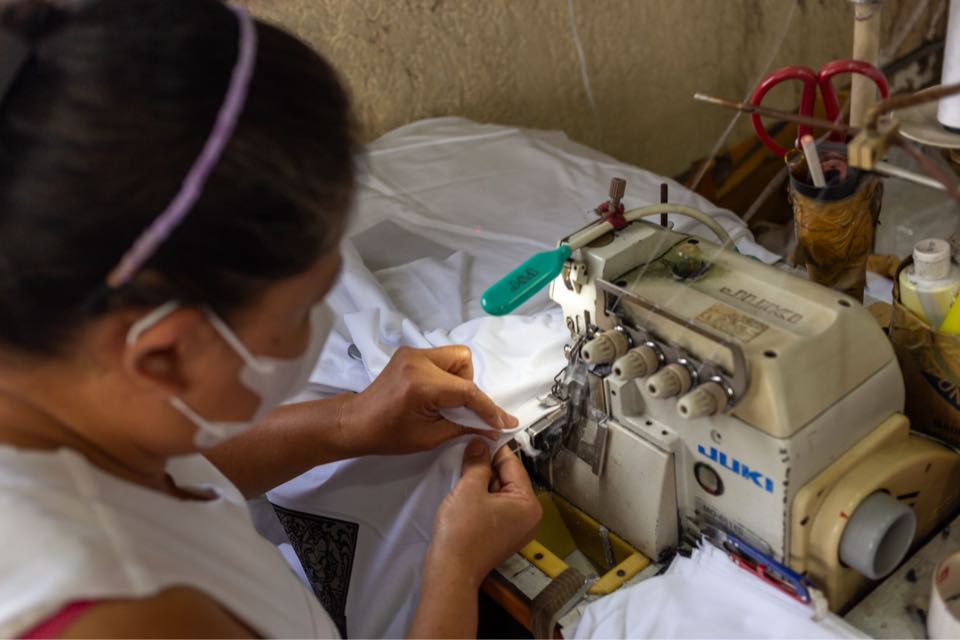 Close-up of an operator in a face mask guiding white fabric through an overlock machine.