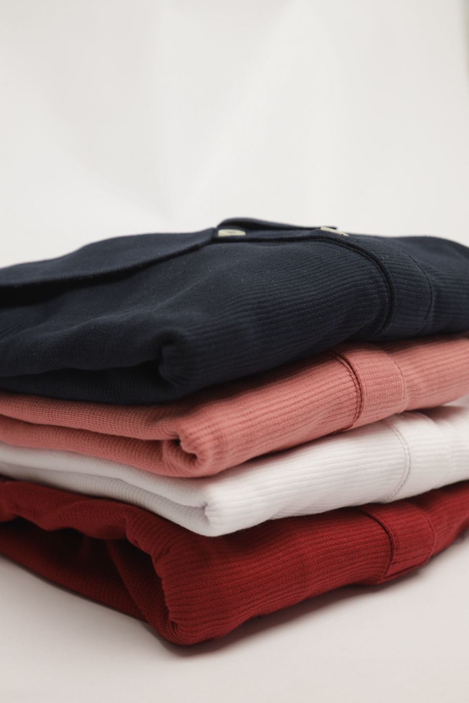 Folded polo shirts stacked in navy, coral pink, white and red.