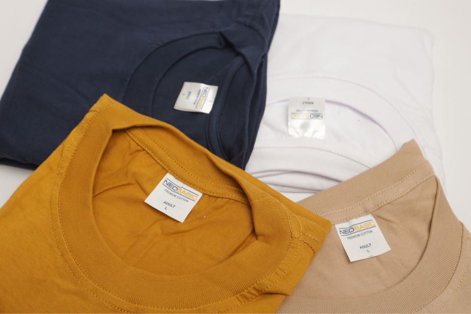 Folded crew-neck tees in navy, mustard, white and sand, each showing a Neobasic neck label.